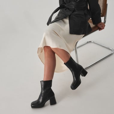 Claudia black patent leather platform boot, perspective view, wide shot of model sitting on a chair - MONPIEL 2