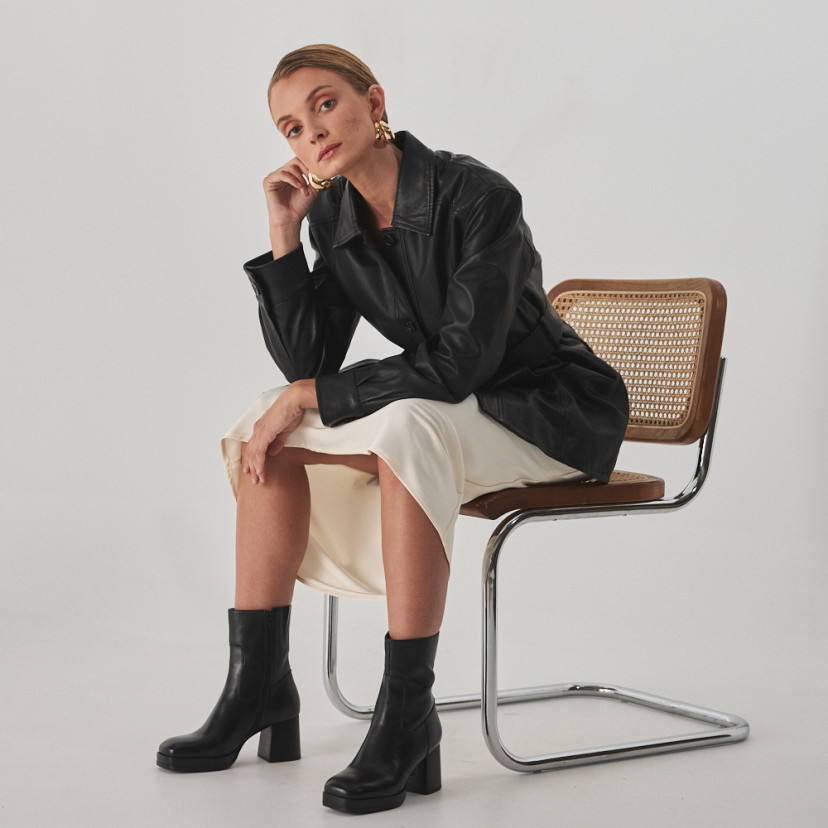 Claudia platform boot in black, perspective view, model sitting on the chair - MONPIEL
