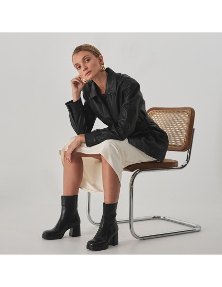 Claudia platform boot in black, perspective view, model sitting on the chair - MONPIEL Claudia platform boot in black, perspective view, model sitting on the chair - MONPIEL