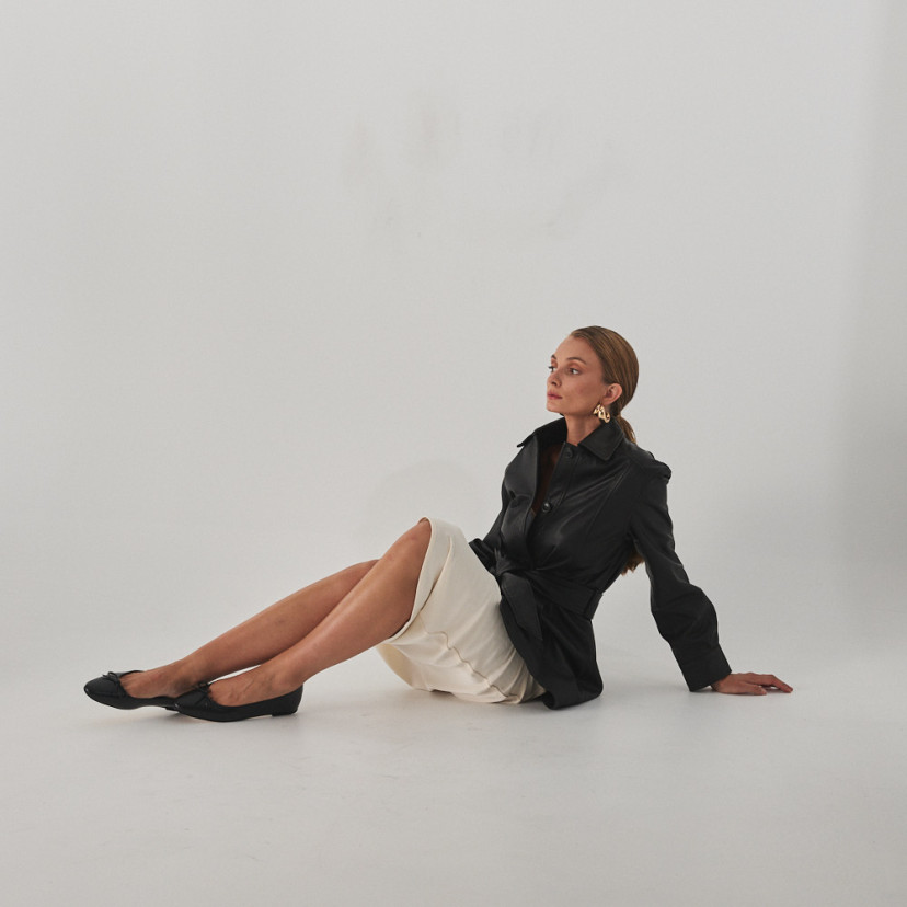 Manolita flat ballerina with stylized toe in black, full shot of model sitting on the floor - MONPIEL