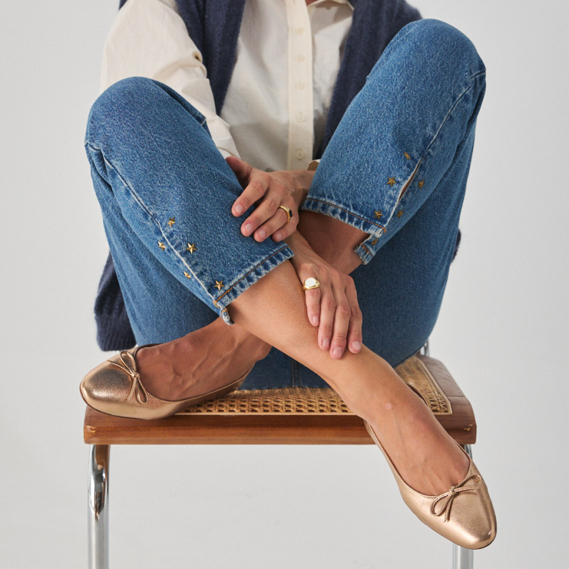 Manolita flat ballerina with stylized toe in metallic color, model sitting on the chair with crossed legs, front view - MONPIEL