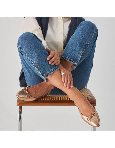 Manolita flat ballerina with stylized toe in metallic color, model sitting on the chair with crossed legs, front view - MONPIEL Manolita flat ballerina with stylized toe in metallic color, model sitting on the chair with crossed legs, front view - MONPIEL