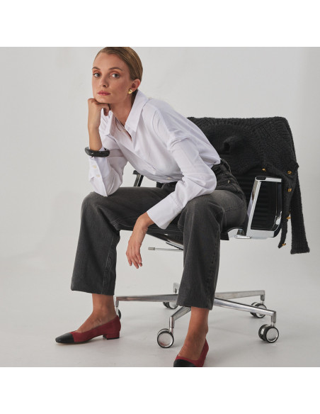 Sapato feminino com ponta quadrada de couro em rosa camurça e bico preto, modelo sentada na cadeira plano geral - MONPIEL Sapato feminino com ponta quadrada de couro em rosa camurça e bico preto, modelo sentada na cadeira plano geral - MONPIEL