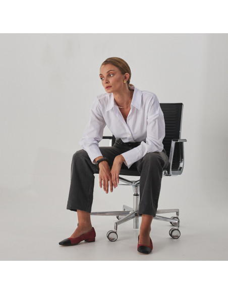 Women's shoe with square toe in pink suede leather and black toe cap, model sitting on the chair, wide shot - MONPIEL