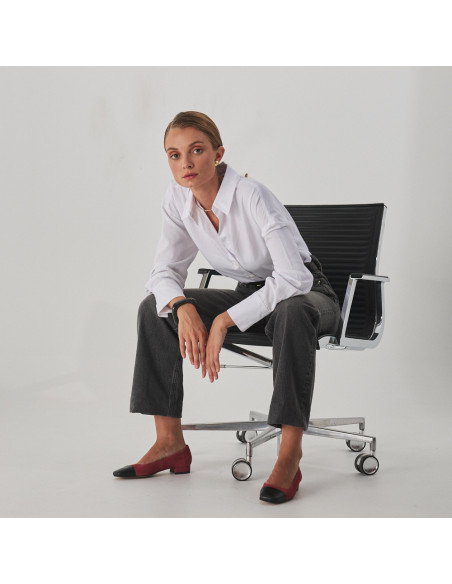 Sapato feminino com ponta quadrada de couro em rosa camurça e bico preto, modelo sentada na cadeira plano geral - MONPIEL Sapato feminino com ponta quadrada de couro em rosa camurça e bico preto, modelo sentada na cadeira plano geral - MONPIEL