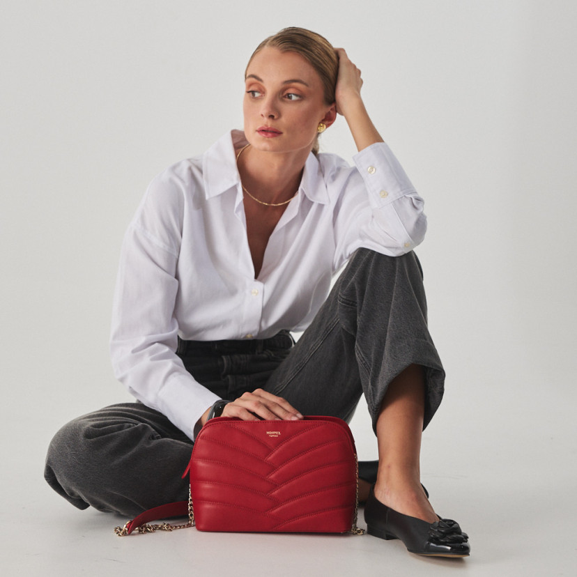 Bolsa acolchoada de couro com corrente dourada na cor vermelha apoiada no chão e modelo sentada - MONPIEL