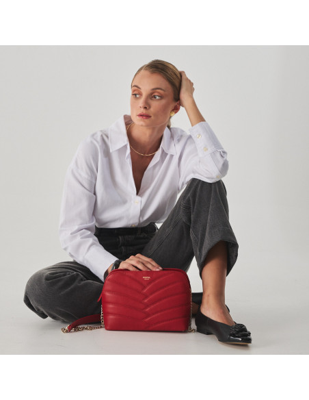 Bolsa acolchoada de couro com corrente dourada na cor vermelha apoiada no chão e modelo sentada - MONPIEL Bolsa acolchoada de couro com corrente dourada na cor vermelha apoiada no chão e modelo sentada - MONPIEL