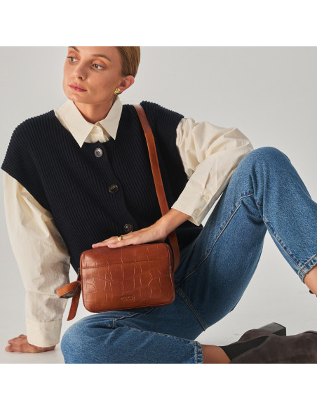 Crocodile leather crossbody bag in brown, with crossbody handle held with hands, model sitting on the floor - MONPIEL