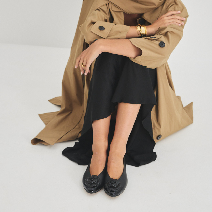 Ameliè patent leather ballerina with flower toe in black, front view, bent knees, model sitting on the floor - MONPIEL
