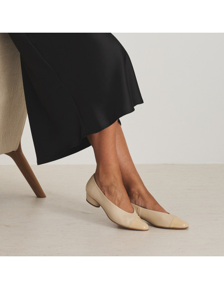 Bicolor-Spitzen-Ballerina mit Absatz aus beige/lackbeigem Leder, Profilansicht, Modell sitzt im Sessel - MONPIEL Bicolor-Spitzen-Ballerina mit Absatz aus beige/lackbeigem Leder, Profilansicht, Modell sitzt im Sessel - MONPIEL