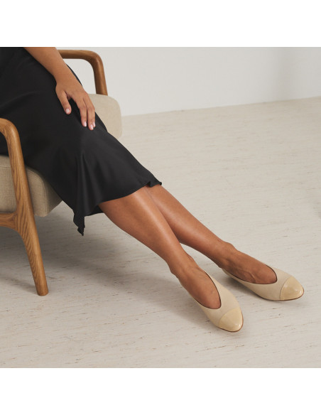 Bicolor-Spitzen-Ballerina mit Absatz aus beige/lackbeigem Leder, Modell sitzt auf einem Stuhl, Beine seitlich gekreuzt - MONPIEL Bicolor-Spitzen-Ballerina mit Absatz aus beige/lackbeigem Leder, Modell sitzt auf einem Stuhl, Beine seitlich gekreuzt - MONPIEL