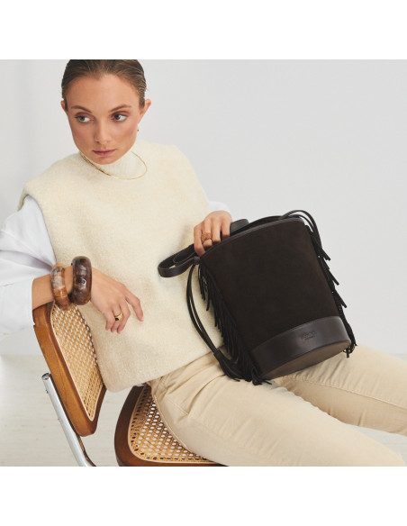 Borsa a secchiello grande in pelle scamosciata marrone con frange, appoggiata sopra le gambe - MONPIEL