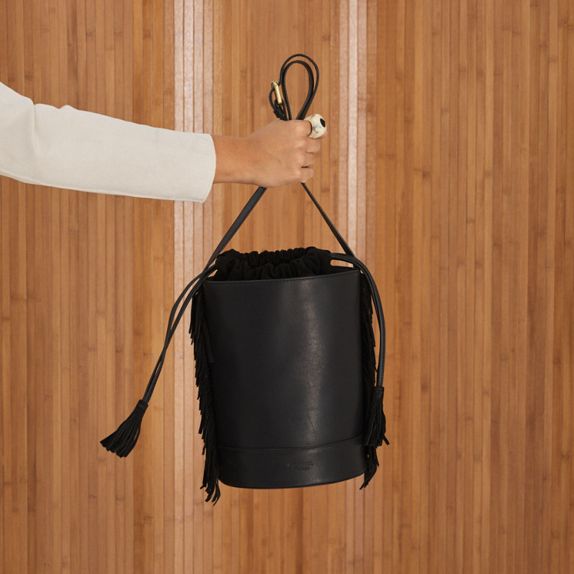 Bolsa bucket grande em couro preto com franjas, segurada na mão, pendurada, vista frontal - MONPIEL