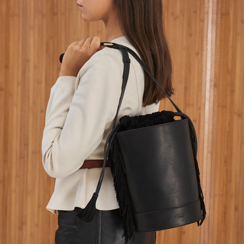 Bolsa bucket grande em couro preto com franjas, pendurada nas costas, plano médio - MONPIEL