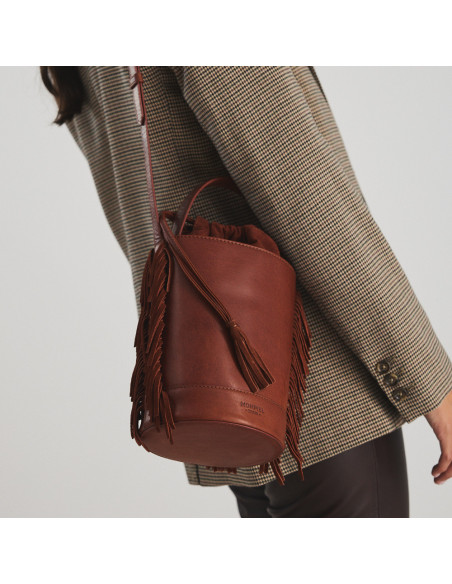 Große Leder-Bucket-Bag mit Fransen in der Farbe Cognac, über die Schulter getragen, Nahaufnahme - MONPIEL