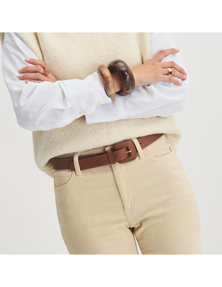 Brown leather belt with covered buckle, worn over corduroy pants, model with arms crossed - MONPIEL Brown leather belt with covered buckle, worn over corduroy pants, model with arms crossed - MONPIEL