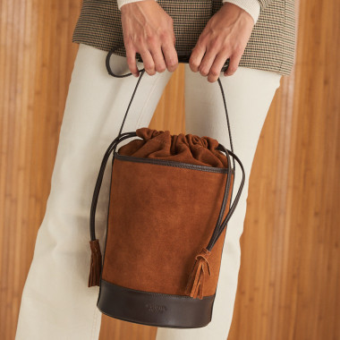 Sac rond en forme de seau de couleur havane, vue de face posé sur un meuble, avec un miroir en arrière-plan - MONPIEL 2