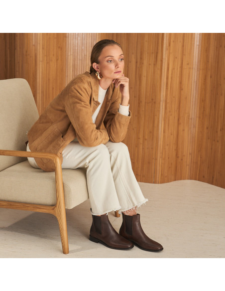 Luisa Chelsea ankle boot in brown leather with perspective view, wide shot of the model sitting sideways on the chair - MONPIEL Luisa Chelsea ankle boot in brown leather with perspective view, wide shot of the model sitting sideways on the chair - MONPIEL