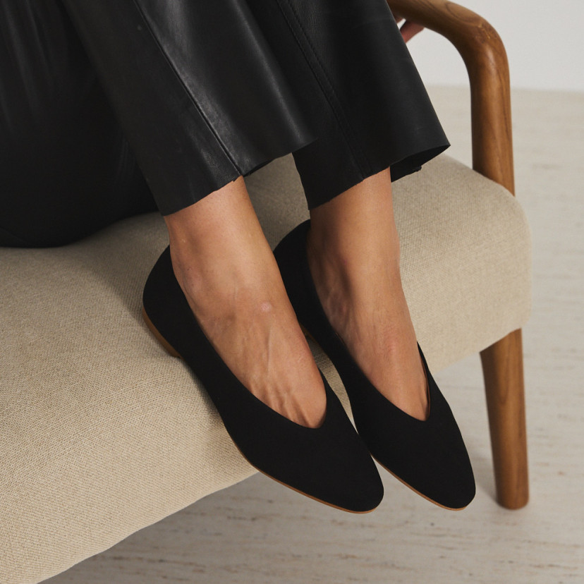 Flat ballerina in black suede with feet raised on the armchair and zoomed-in perspective view - MONPIEL