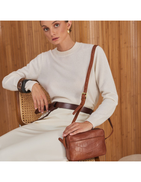 Coco leather crossbody bag in tan, with long strap over the shoulder, model sitting on the chair - MONPIEL