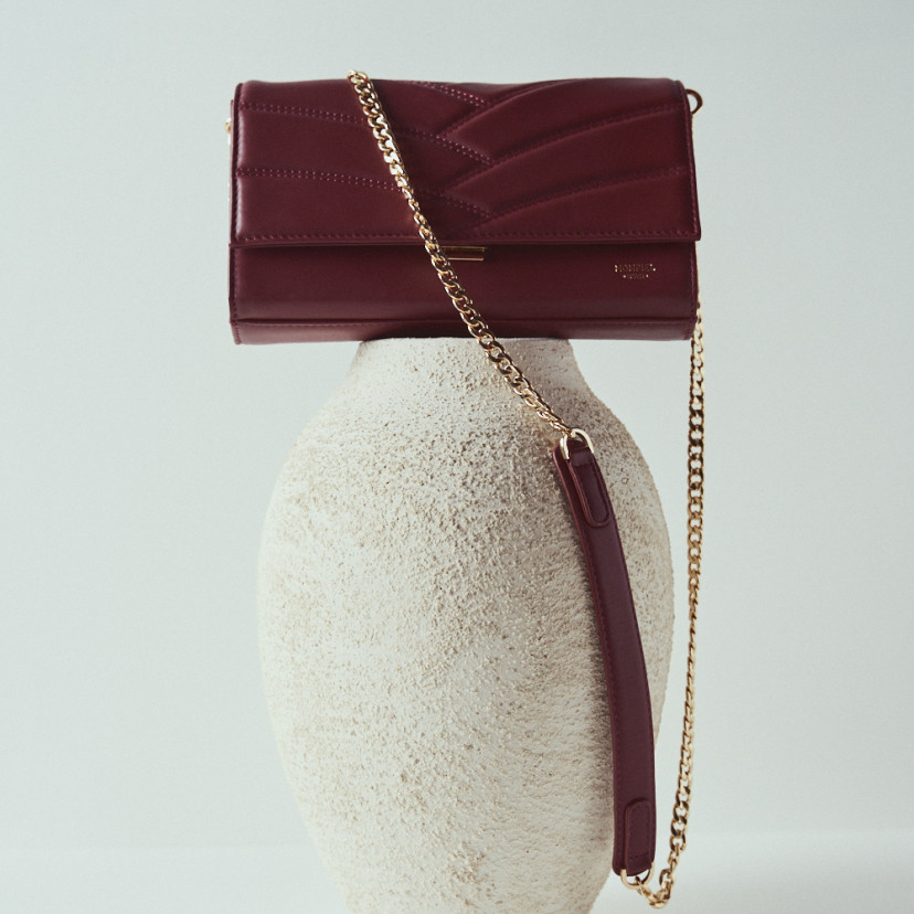 Venice women’s leather clutch bag in burgundy with front view on top of a vase - MONPIEL