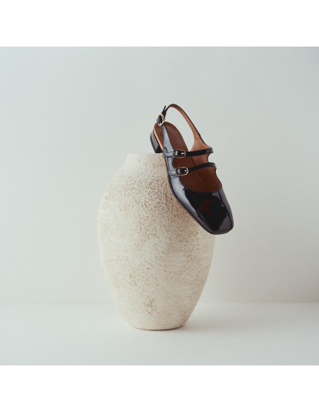 Mary Jane sans talon Lolina en cuir noir, talon reposant sur un vase, fond blanc - MONPIEL Mary Jane sans talon Lolina en cuir noir, talon reposant sur un vase, fond blanc - MONPIEL