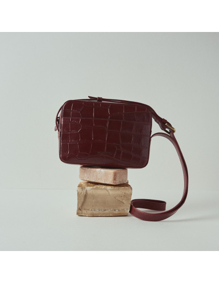 Sac bandoulière en cuir coco couleur bordeaux, vue frontale posé sur du savon - MONPIEL Sac bandoulière en cuir coco couleur bordeaux, vue frontale posé sur du savon - MONPIEL