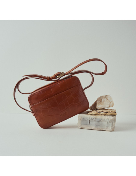 Borsa a tracolla in pelle coco color cuoio inclinata, vista frontale appoggiata su una roccia - MONPIEL Borsa a tracolla in pelle coco color cuoio inclinata, vista frontale appoggiata su una roccia - MONPIEL