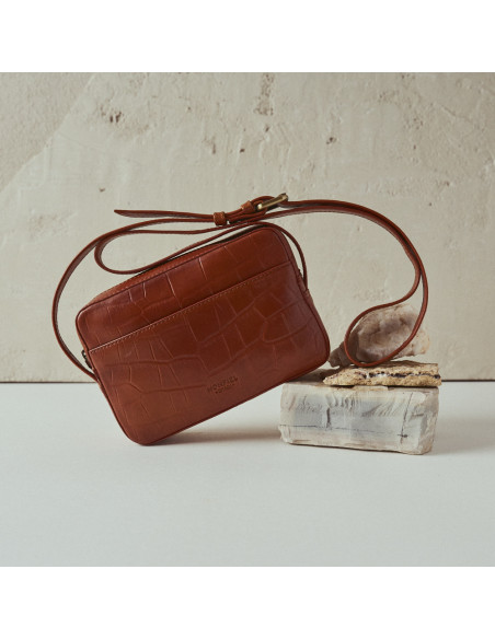 Bolso bandolera de piel coco en color cuero inclinado, con vista frontal, apoyado sobre roca - MONPIEL Bolso bandolera de piel coco en color cuero inclinado, con vista frontal, apoyado sobre roca - MONPIEL