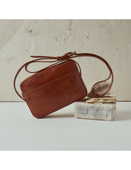 Borsa a tracolla in pelle coco color cuoio inclinata, vista frontale appoggiata su una roccia - MONPIEL Borsa a tracolla in pelle coco color cuoio inclinata, vista frontale appoggiata su una roccia - MONPIEL