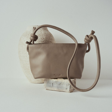 Petit sac en cuir avec nœuds couleur taupe, vue de face, détail de la anse, posé sur une roche - MONPIEL