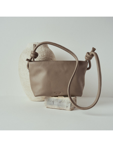 Bolsa pequena de couro com nós na cor taupe, vista frontal e detalhe da alça, apoiada sobre uma rocha - MONPIEL