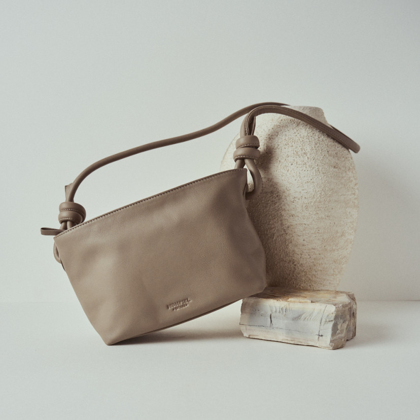 Bolsa pequena de couro com nós na cor taupe, vista frontal e bolsa inclinada apoiada sobre uma rocha - MONPIEL