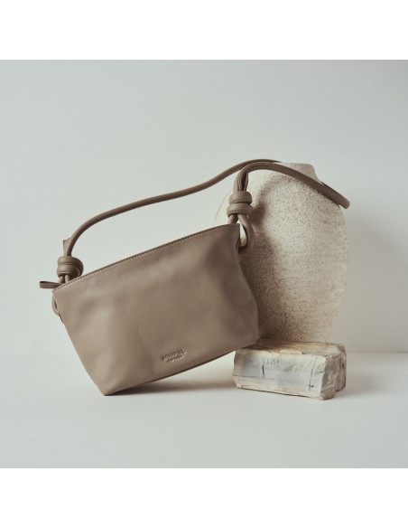 Bolsa pequena de couro com nós na cor taupe, vista frontal e bolsa inclinada apoiada sobre uma rocha - MONPIEL