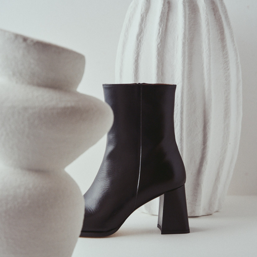 Black leather heeled boot with side view between vases - MONPIEL