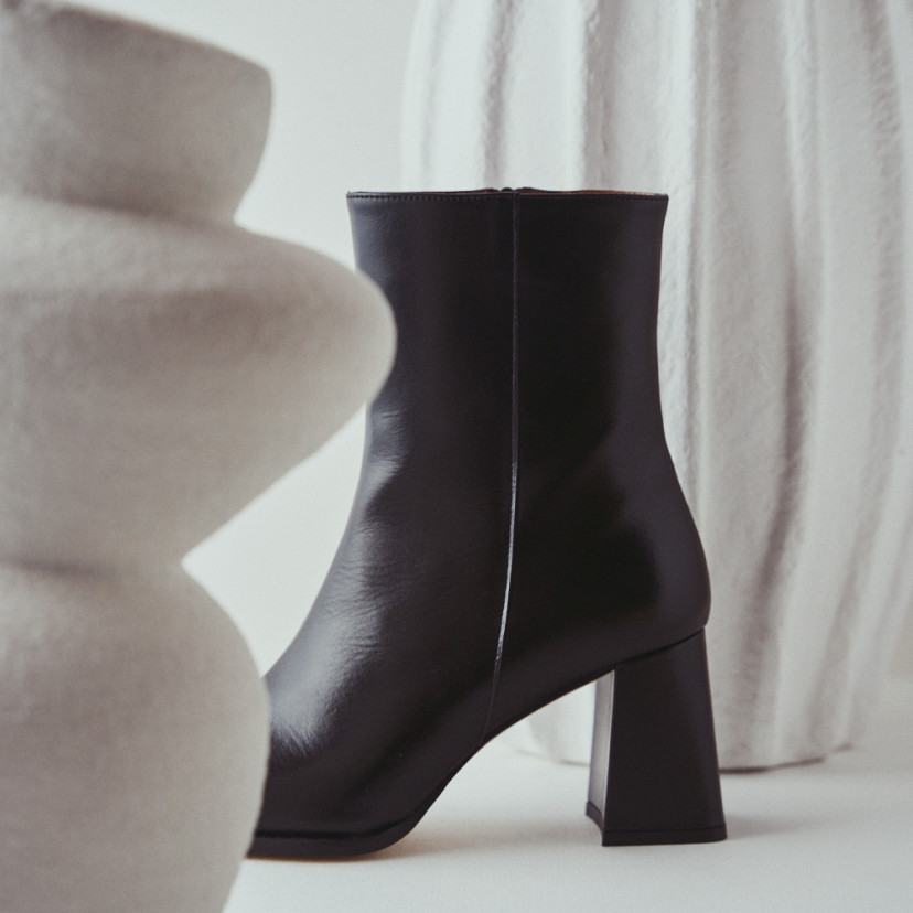 Black leather heeled boot with side view between vases in close-up - MONPIEL