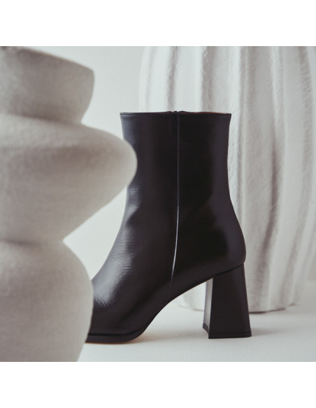 Black leather heeled boot with side view between vases in close-up - MONPIEL Black leather heeled boot with side view between vases in close-up - MONPIEL