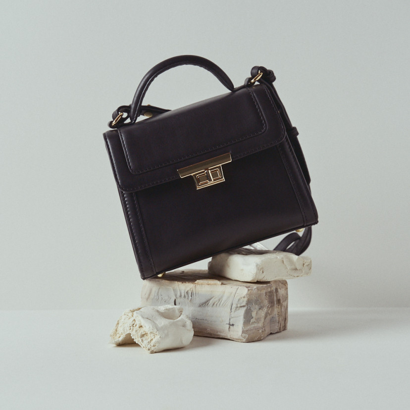 Bolsa de couro feminina 60's na cor preta, vista frontal apoiada em pedras - MONPIEL