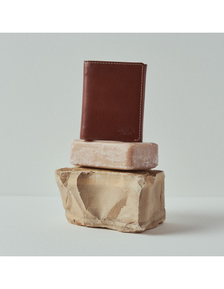 Piccola portafoglio da uomo in pelle con portamonete e portabanconote, colore habana, vista frontale su sapone e rocci - MONPIEL