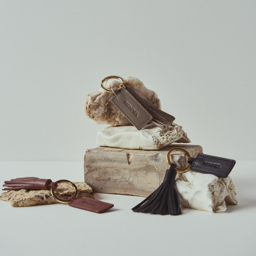 Leather tassel keychain in black, taupe, and leather color between rocks - MONPIEL
