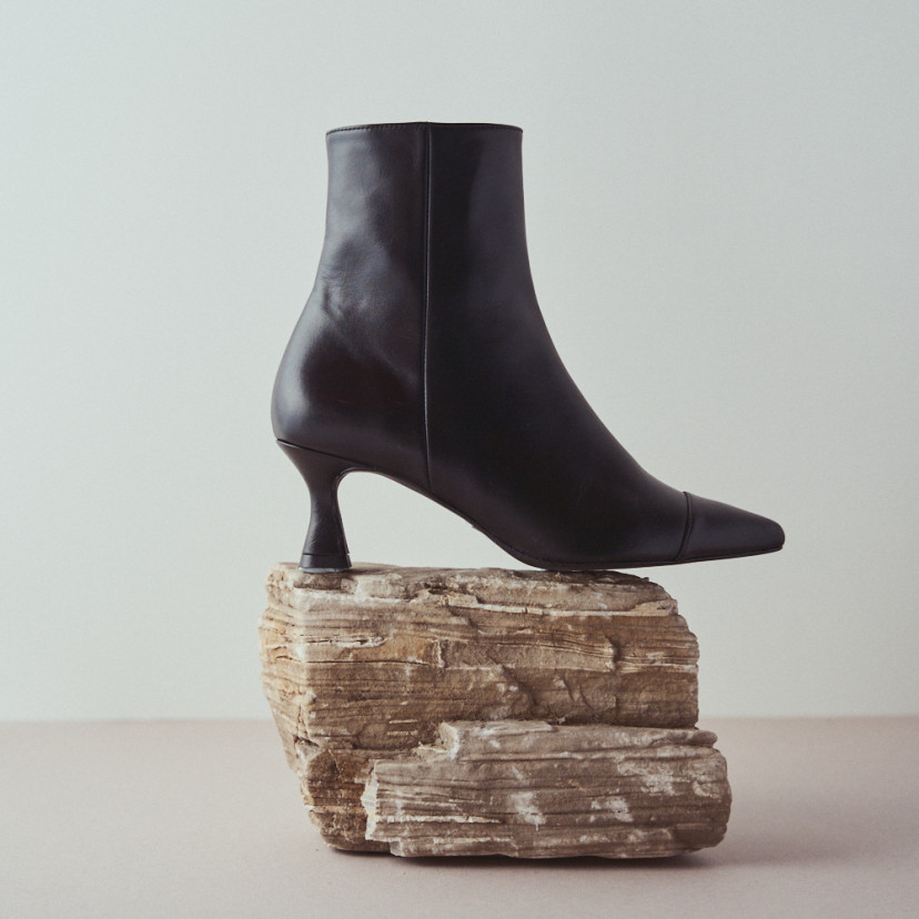 Jimena pointed-toe leather boot in black with side view resting on a rock in close-up - MONPIEL