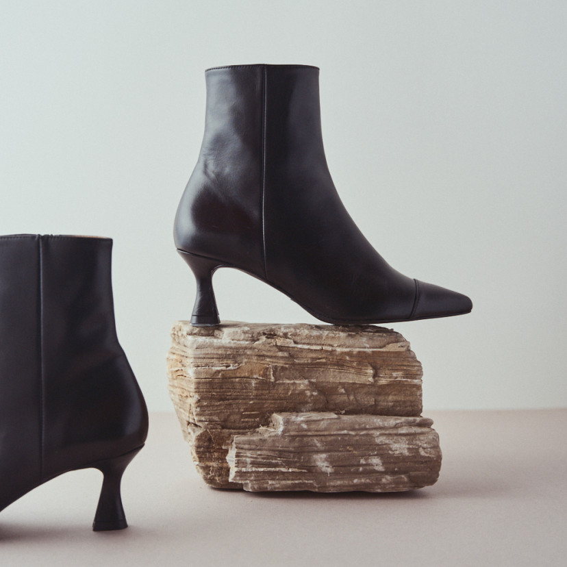 Jimena pointed-toe leather boot in black with side view resting on a rock in close-up - MONPIEL