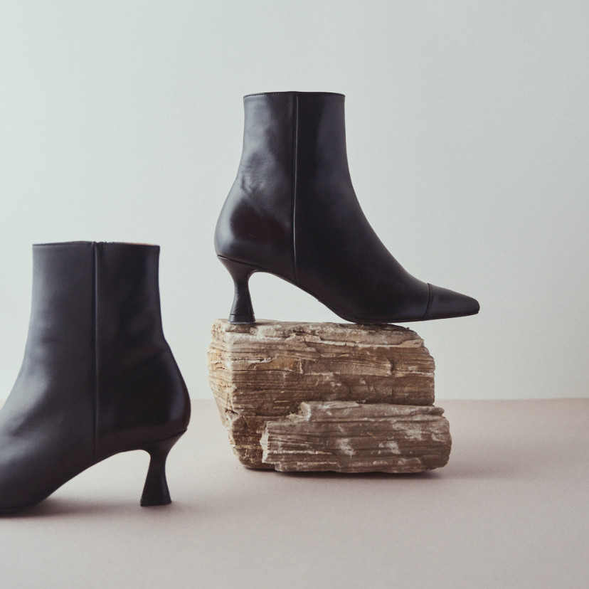 Jimena pointed-toe leather boot in black with side view resting on a rock, the other boot next to it - MONPIEL