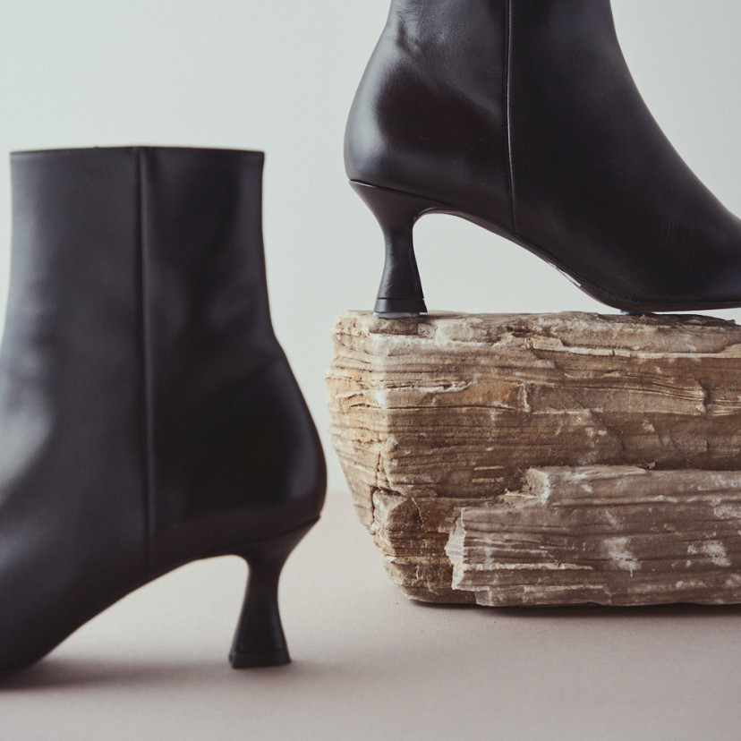 Jimena pointed-toe leather boot in black with side view resting on a rock, heel detail in close-up - MONPIEL