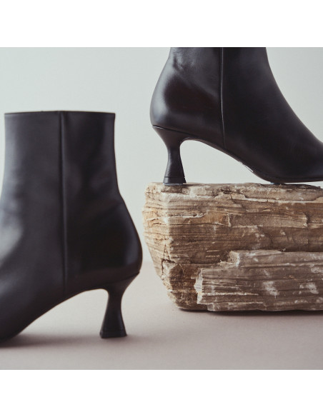 Black pointed-toe Jimena leather boot, profile view, resting on a rock, close-up detail of the heel - MONPIEL Black pointed-toe Jimena leather boot, profile view, resting on a rock, close-up detail of the heel - MONPIEL