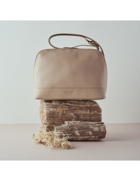 Bolso mediano de piel en color beige con vista frontal apoyado sobre una roca - MONPIEL Bolso mediano de piel en color beige con vista frontal apoyado sobre una roca - MONPIEL