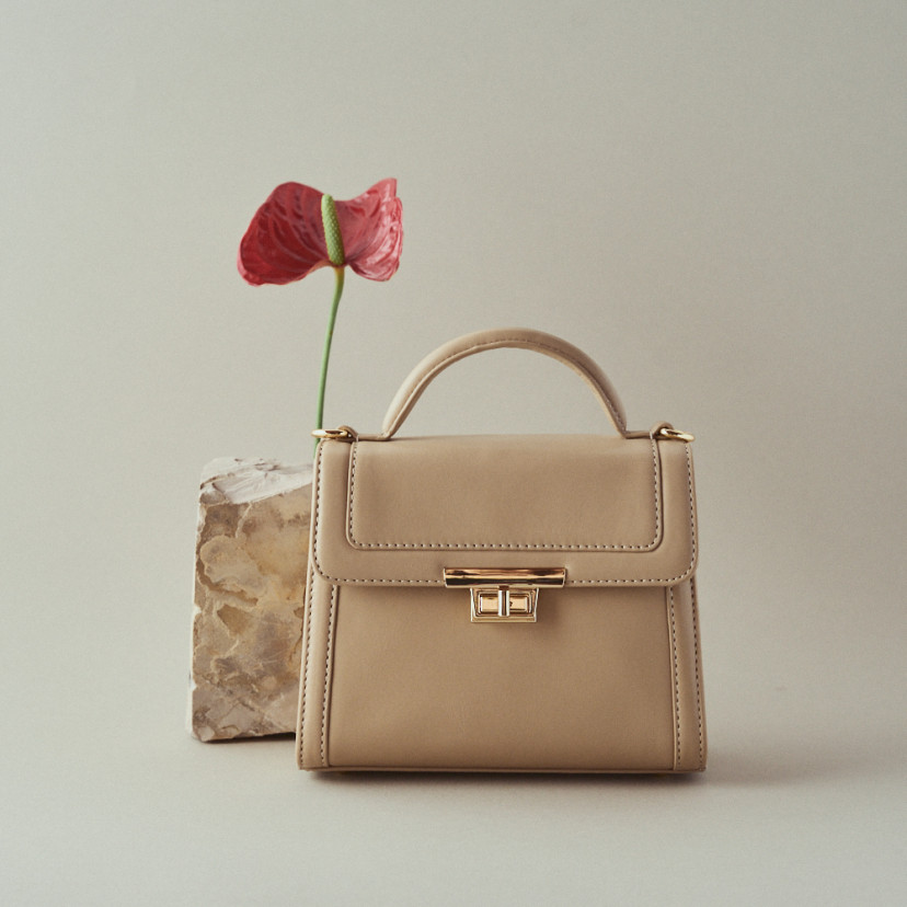Small 60's leather women's bag in beige with front view next to a flower - MONPIEL
