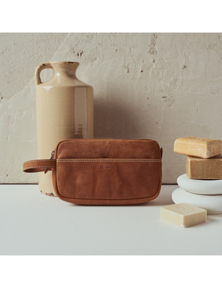 Necessaire masculino de couro na cor habana, vista frontal apoiado sobre um vaso - MONPIEL Necessaire masculino de couro na cor habana, vista frontal apoiado sobre um vaso - MONPIEL