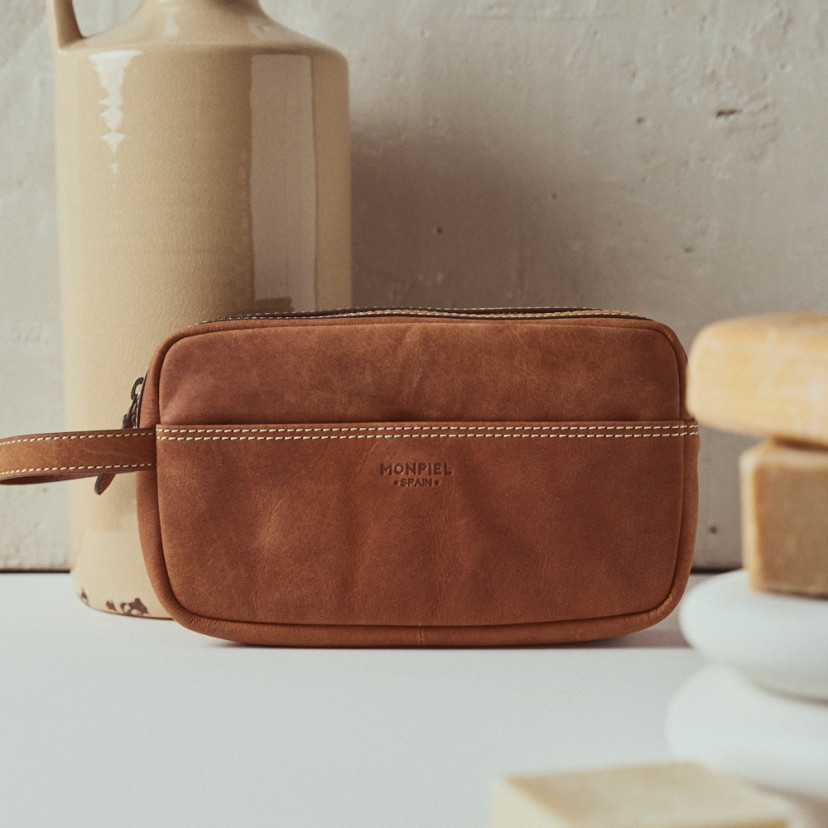 Men's leather toiletry bag in Havana colour with logo detail, front view over a vase - MONPIEL