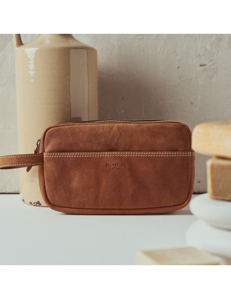 Necessaire masculino de couro na cor habana com detalhe do logo, vista frontal apoiado sobre um vaso - MONPIEL Necessaire masculino de couro na cor habana com detalhe do logo, vista frontal apoiado sobre um vaso - MONPIEL
